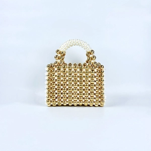 Detail of handmade beaded handbag featuring gold metal beads and white pearl top handle