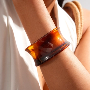 Macro detail of wide acrylic cuff with amber tortoise shell pattern on a white fabric background