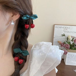 Detail of red cherry hair clip with green bow styled on a braided hairstyle