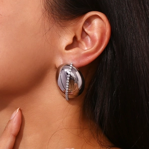 Macro shot of a silver pebble-shaped earring with white zircon inlay on a female model