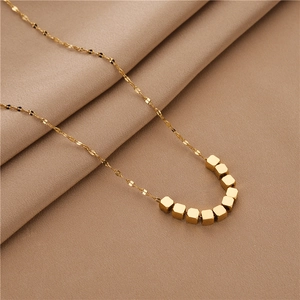 Polished gold square cube necklace on beige fabric, elegant minimalist clavicle chain