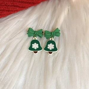 Detail of Christmas earrings featuring green bows and snowflake patterned bells on faux fur