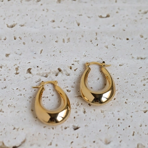 Detail view of thick gold oval hoop earrings on a textured natural stone background