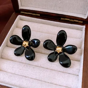 Boucles d'oreilles fleurs noires élégantes avec centre doré sur un écrin de luxe