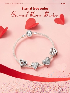 Macro detail of silver charm bracelet with hollow heart pendants and snake chain design