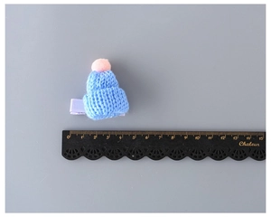 Detailed view of mini light blue knitted hat hair clip with pink pompom and size ruler