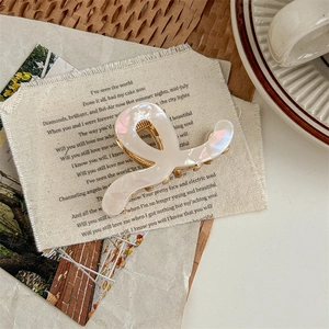 Macro view of white pearlescent acetate wave hair claw clip with golden metal base