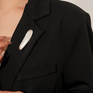 Close-up of minimalist white oblong metal brooch pinned on a black tailored suit jacket