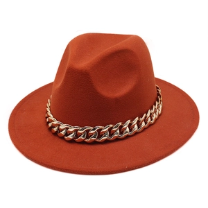 Detail of a rust orange wool fedora hat featuring a chunky gold chain embellishment