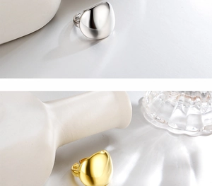 Anelli aperti lucidi in argento e oro con design a goccia liscia su superficie bianca