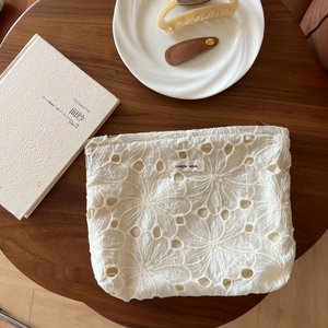 Detail of delicate lace floral embroidery on a white mesh makeup bag with simple wish label