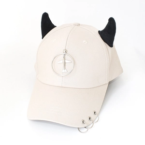 Detail of off-white baseball cap featuring black demon horns and metal ring aircraft charm