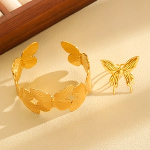 Detail view of the golden butterfly bracelet and ring set on a neutral textured surface