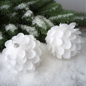 Macro detail of white petal-patterned Christmas balls with glitter on snowy pine branches