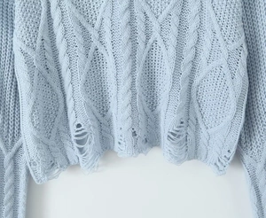 Detail of light blue cable knit sweater featuring trendy distressed hem and soft fiber texture