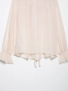 Detail of pink chiffon blouse featuring polka dot patterns and ruffled cuffs with a tie-up waist