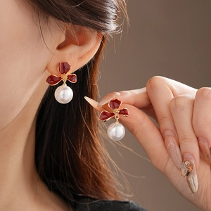 Detailed close-up of red enamel flower earrings with white pearl drop on female ear