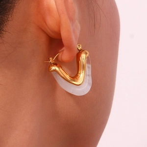 Close-up of golden geometric V-shaped earrings with white acrylic on a model's ear