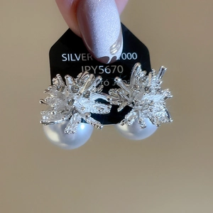 Close-up of floral silver earrings with white pearls on a black display card
