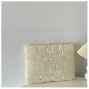 Close-up of beige quilted laptop sleeve showing soft padded texture and zipper detail