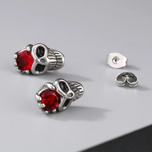 Detailed view of silver skull stud earrings with sparkling red gemstone eyes