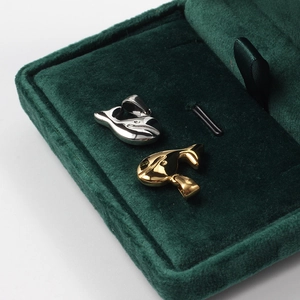 Detailed view of silver and gold whale pendants resting in a green velvet jewelry box