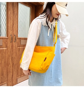 Outdoor shot of a bright yellow canvas crossbody bag on a model with minimalist style
