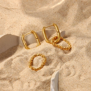 Detailed shot of golden rectangular earrings and twisted ring on natural stone and sand