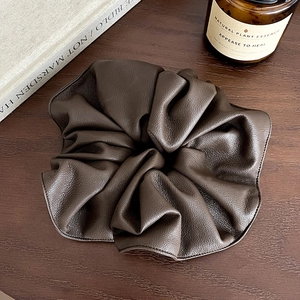 Détail d'un chouchou en similicuir marron foncé avec texture grainée sur bois
