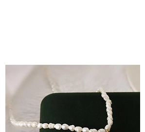 Détail d'un collier de perles baroques avec pendentif cœur doré sur velours vert