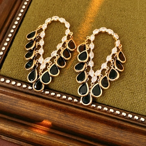 Detailed shot of golden tassel earrings with black teardrop stones on green velvet