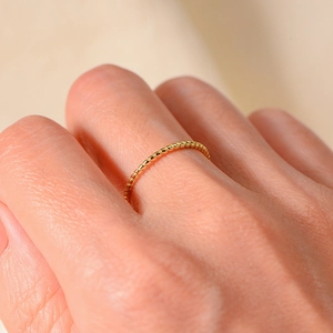 Macro shot of minimalist golden twisted rope ring on finger showing delicate texture
