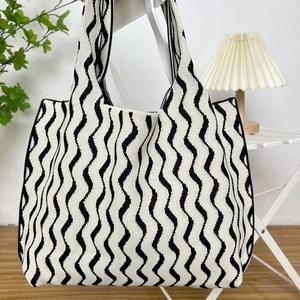 Close-up of black and white wave pattern knit tote bag hanging on a white chair