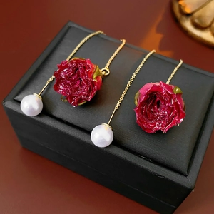 Détail de boucles d'oreilles roses rouges avec perles blanches et chaînes dorées sur boîte