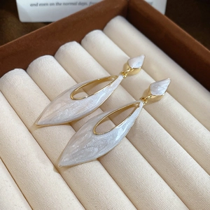 Macro view of gold drop earrings with white marble resin inlay in jewelry box