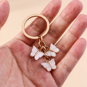 Detail of three white acrylic butterfly charms with pearlescent texture on a gold keyring