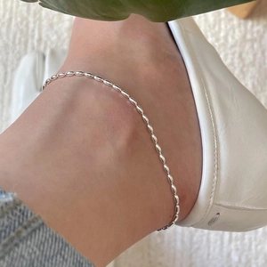 Detail of minimalist S925 sterling silver anklet with olive-shaped beads on ankle