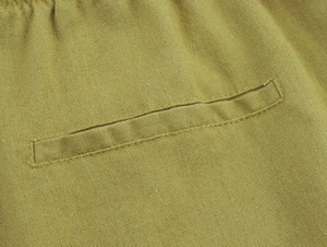 Detailed macro view of a welt pocket on textured linen trousers in mustard khaki color