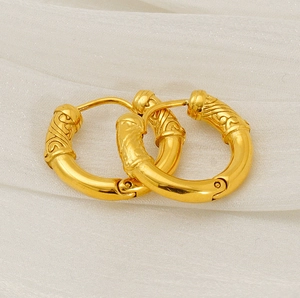 Détail de boucles d'oreilles créoles dorées avec gravures vintage sur un tissu blanc texturé