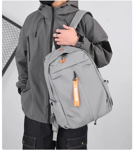 Men's grey business travel backpack shown on model with waterproof material and orange accents