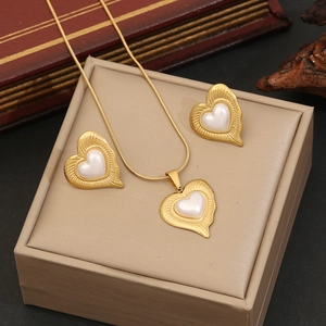 Elegant gold heart jewelry set with white pearls displayed on a beige leather gift box