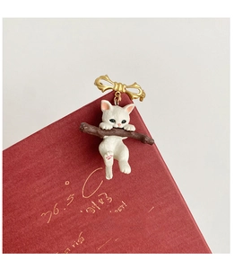 Detail of white kitten brooch on brown branch with a gold bow on a vintage book