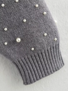 Detailed close-up of grey knitted sleeve cuff featuring elegant white pearl embellishments