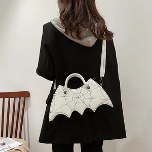 White bat-shaped PU handbag with spiderweb stitching and adjustable shoulder strap worn by model