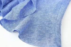 Detail view of blue linen blend fabric with refined stitching and ruffled design
