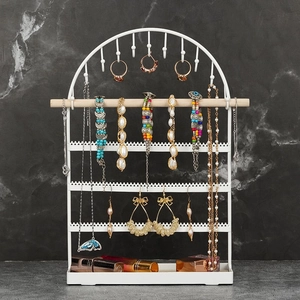White metal jewelry organizer with wooden rods for earrings and necklaces on marble background