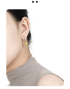 Close-up of a model wearing two-tone rectangular hoop earrings with golden heart charms