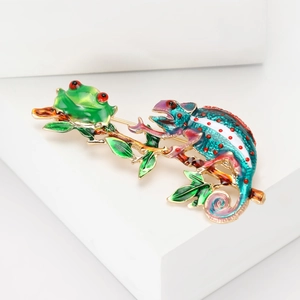 Close-up of enamel frog and chameleon pin on a golden branch with green leaves