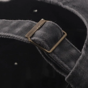 Macro detail of dark grey corduroy cap featuring a bronze metal buckle adjustment strap