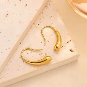 Boucles d'oreilles gouttes dorées polies présentées sur un socle en pierre beige minimaliste